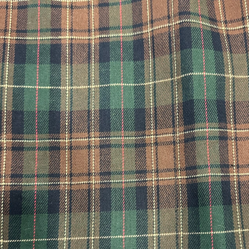 A close-up of a plaid fabric pattern with intersecting green, brown, navy, beige, and thin red lines.