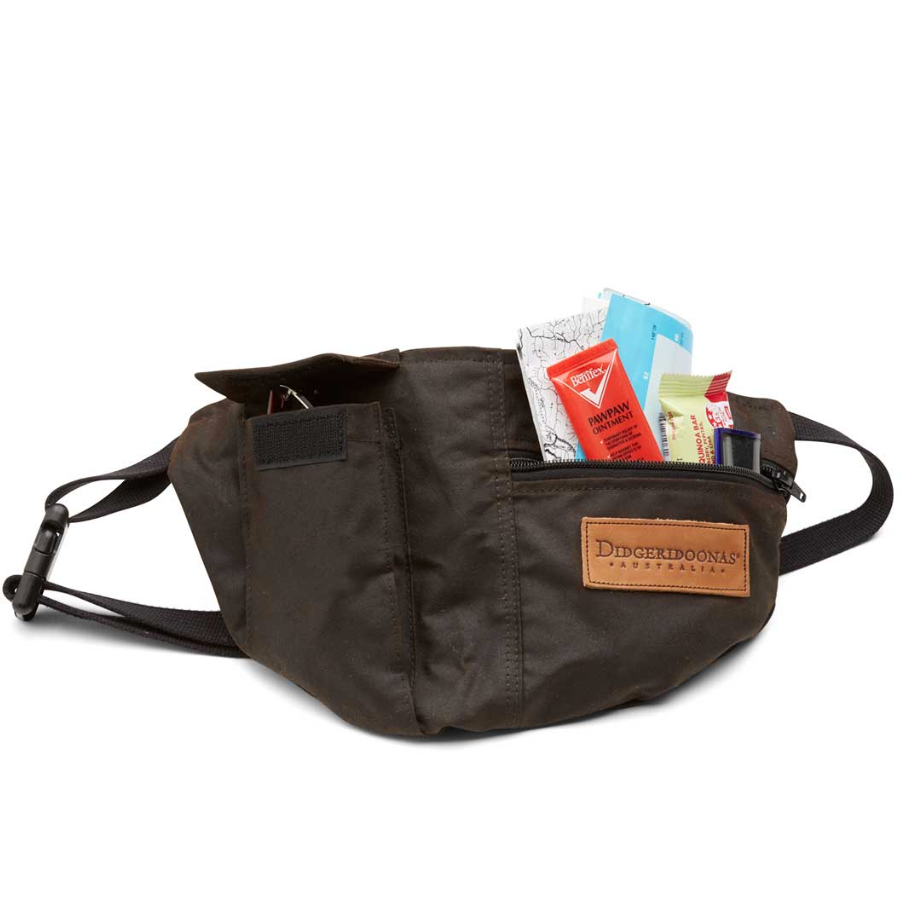 A dark brown Ditchinground fanny pack with a brown leather brand patch, shown with its front zippered pocket open and filled with travel documents, on a white background.