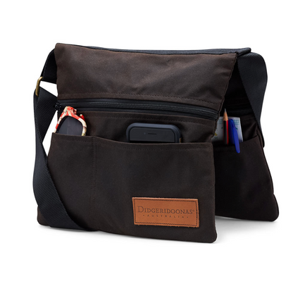 A black canvas shoulder bag with multiple compartments, shown on a white background. The front pocket is open to reveal a smartphone and accessories, and a brown leather brand patch is visible on the front.