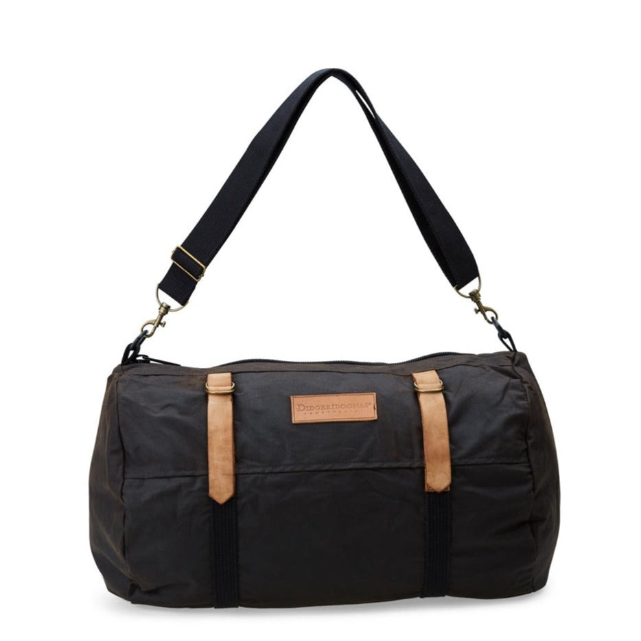 A black oilskin cabin bag with leather straps and an adjustable shoulder strap, featuring a main compartment and two smaller pockets on the back.