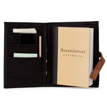 A black oilskin folder with a beige book-like item inside, presumably a notebook or sketchbook. The exterior shows a pen loop, a mobile phone, and a couple of business cards.